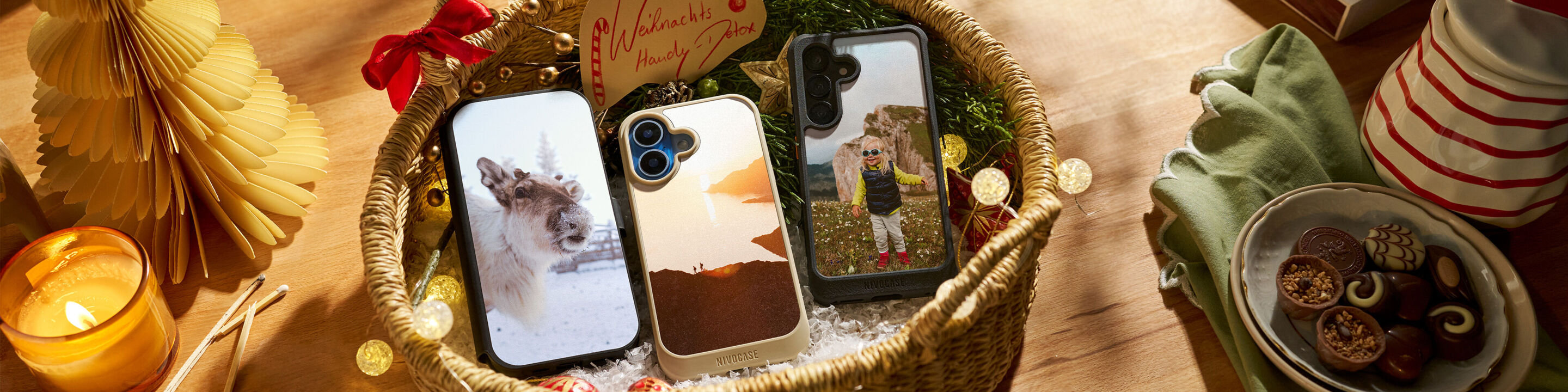 Personalisierte Handyhüllen in einem Geschenkkorb, umgeben von Weihnachtsdekoration.