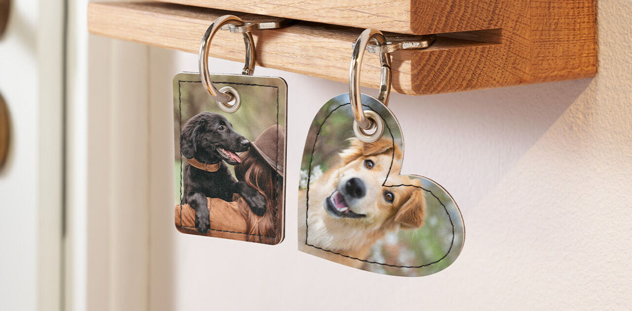 Zwei personalisierte Schlüsselanhänger mit Fotos von Hunden hängen an einem hölzernen Schlüsselbrett.