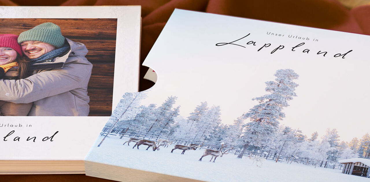 Ein CEWE FOTOBUCH mit Schuber und einer Winterlandschaft aus Lappland mit einem lächelnden Paar.
