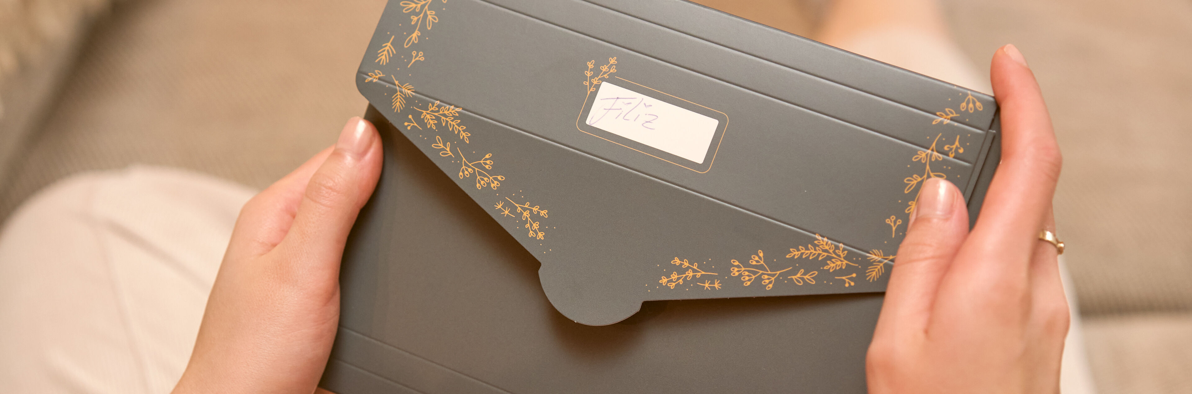 Eine grüne Geschenkverpackung mit goldenen Pflanzendetails, beschriftet mit „Liz“