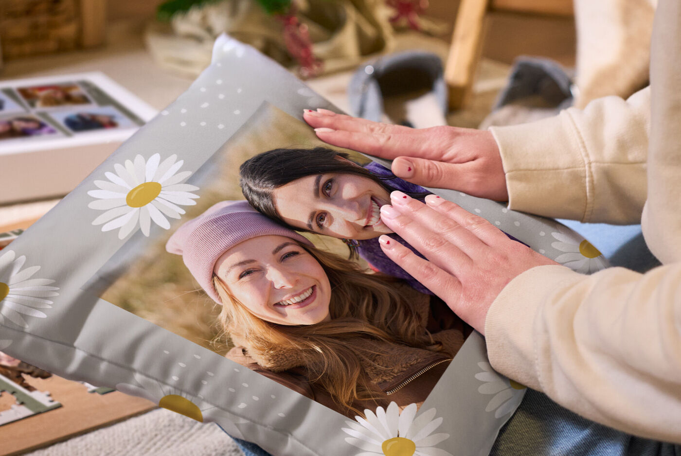 Zwei Hände halten ein graues, bedrucktes Kissen mit Blumenmuster und dem Foto zweier lachender Frauen