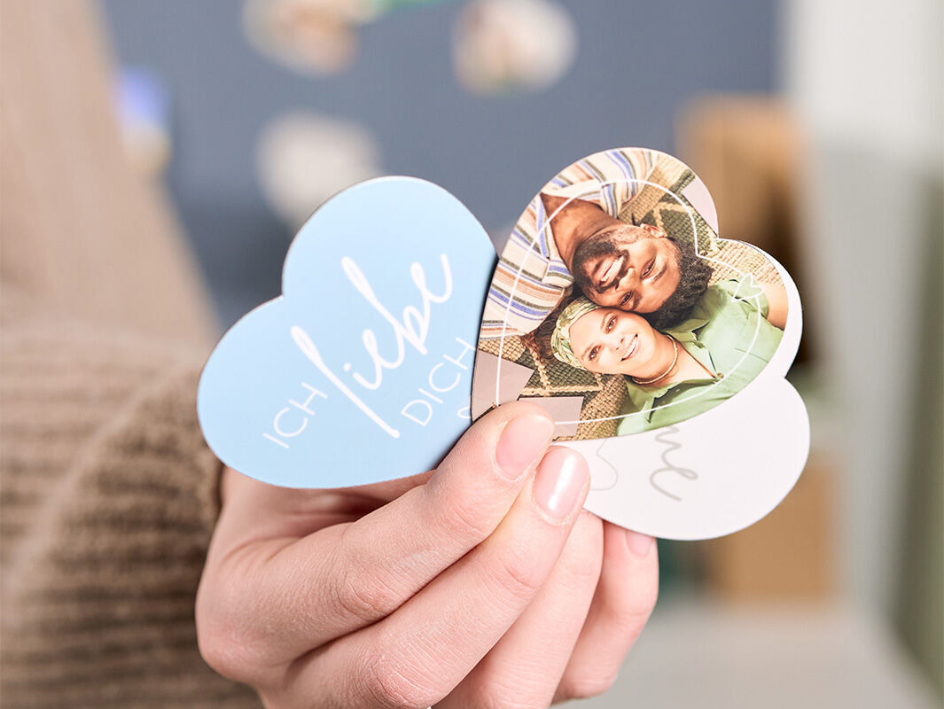 Eine Hand hält drei herzförmige Fotomagnete mit einem Paarfoto und der Aufschrift „Ich liebe Dich“.