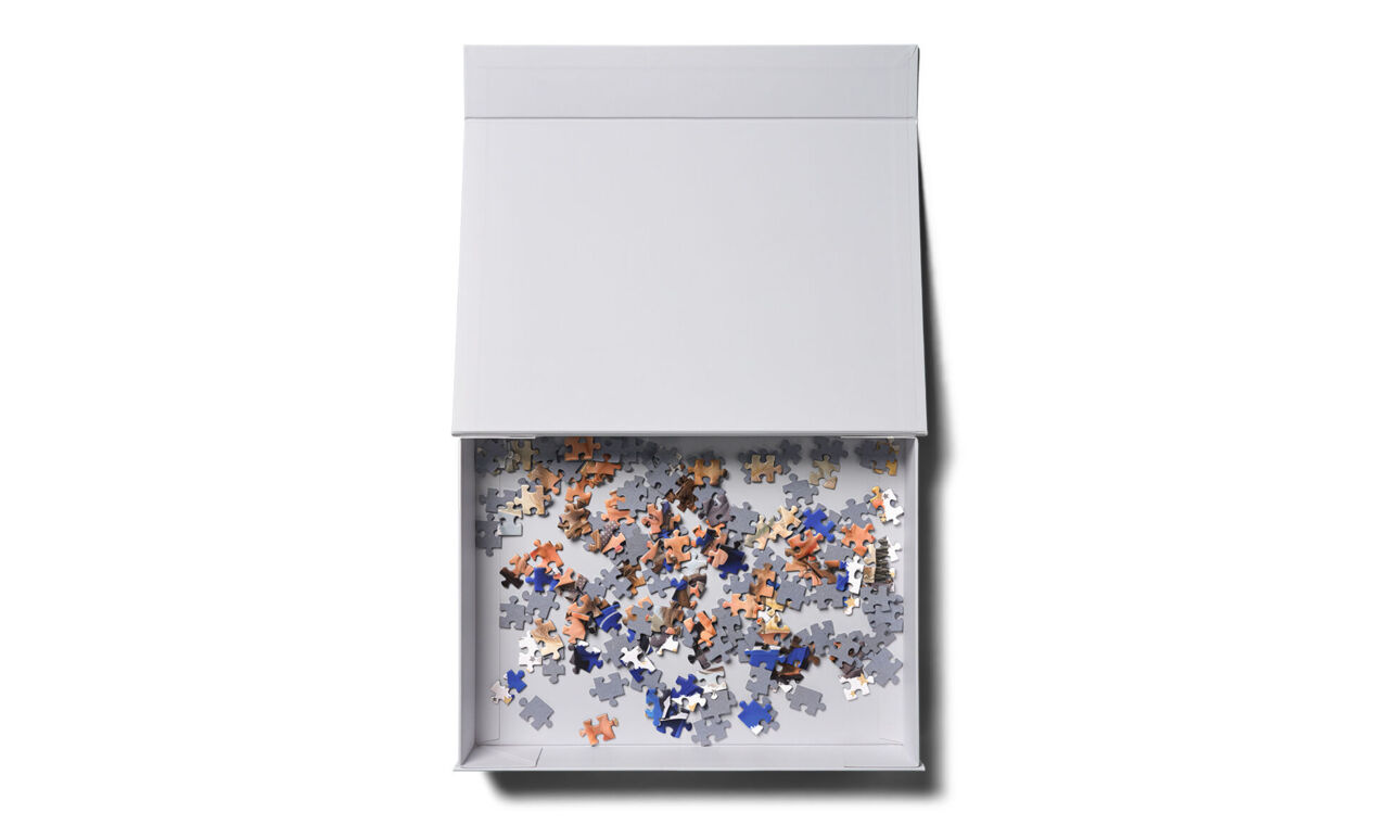 Geöffnete weiße Klappbox mit vielen bunten Puzzleteilen